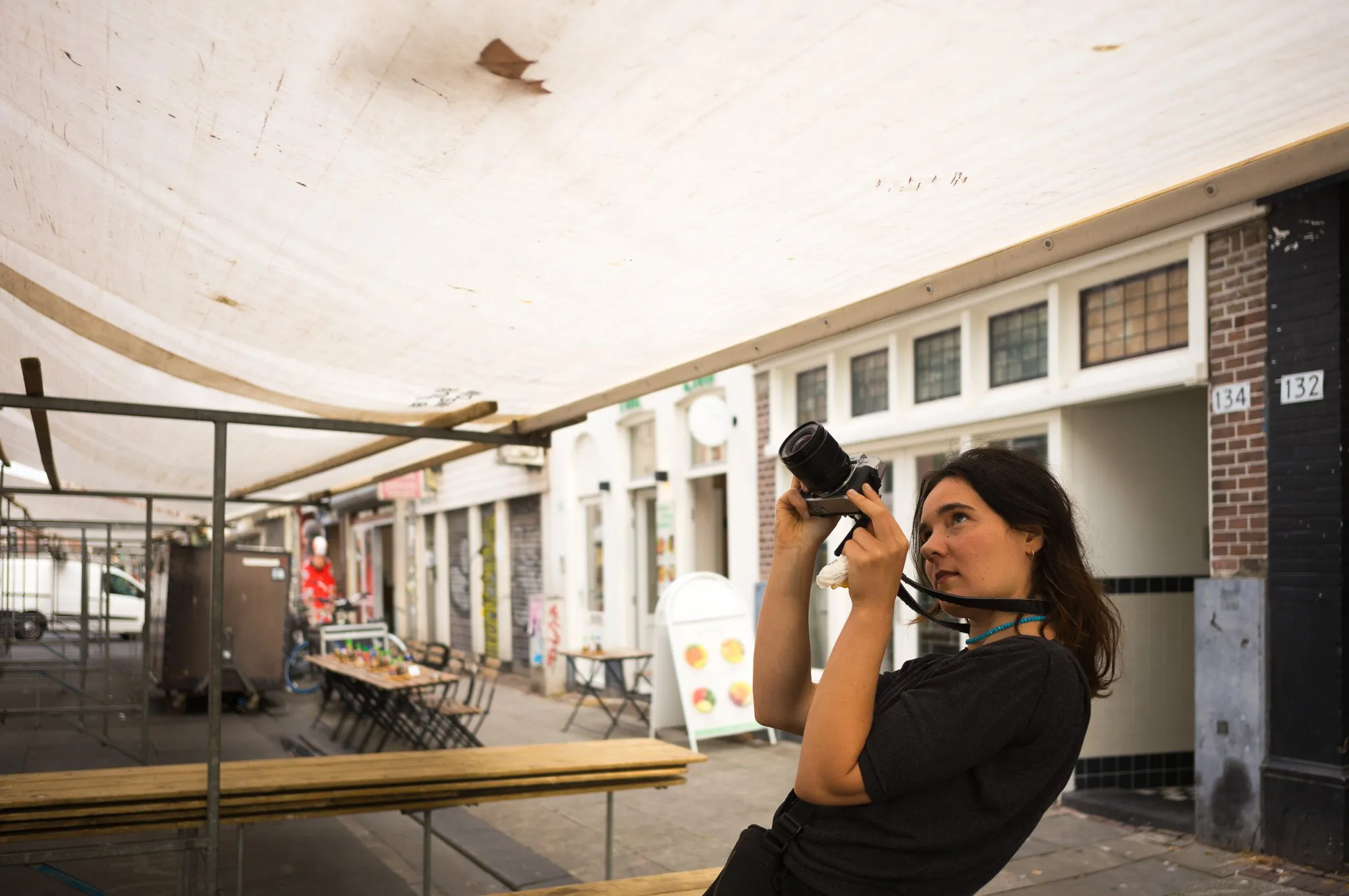 Marie fotografeert op straat in Amsterdam, onder het zeil van een marktkraam
